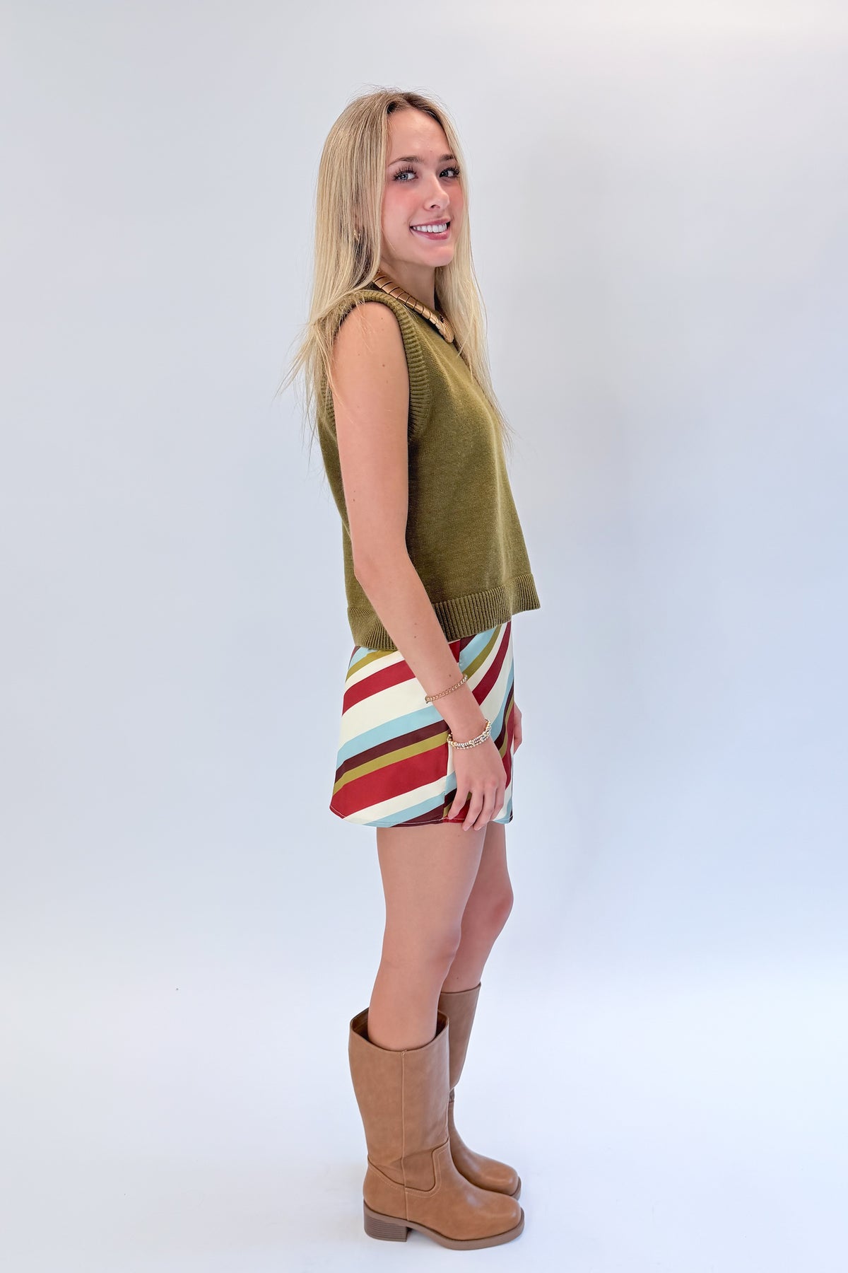 Side view of woman wearing Swagger Boutique’s sweater with Multi Striped Satin Mini Skirt against white studio background.