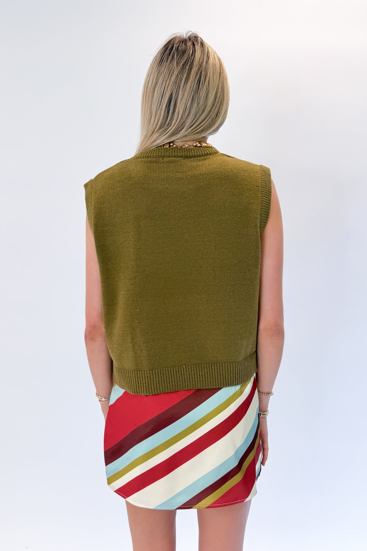 Back view of woman wearing Swagger Boutique’s sweater with Multi Striped Satin Mini Skirt against white studio background.
