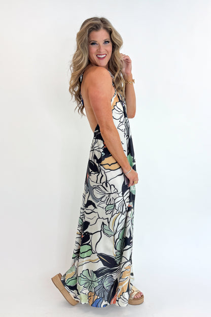 Side view of woman wearing Swagger Boutique’s Multi Tropical Print Halter Neck Maxi with platform sandals against white studio background.