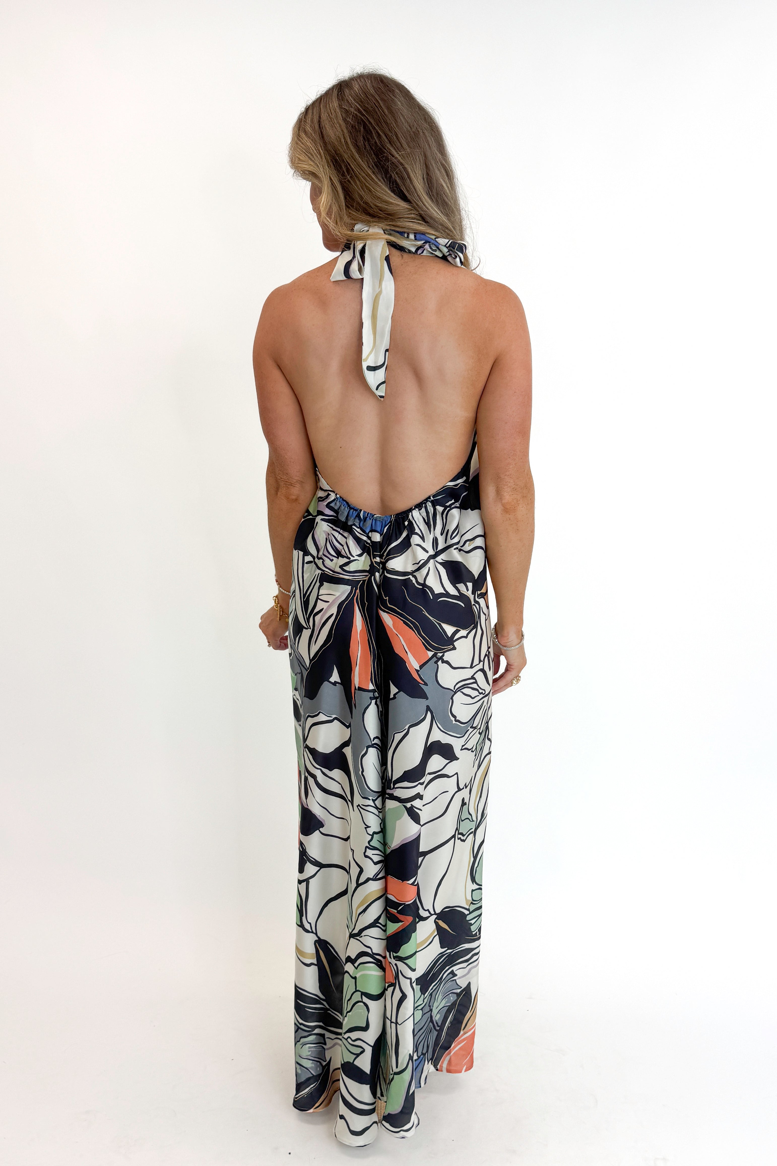 Back view of woman wearing Swagger Boutique’s Multi Tropical Print Halter Neck Maxi with platform sandals against white studio background.