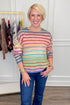 Front view of woman wearing Swagger Boutique’s Multi Striped Sweater with jeans with clothing hanging in the background.