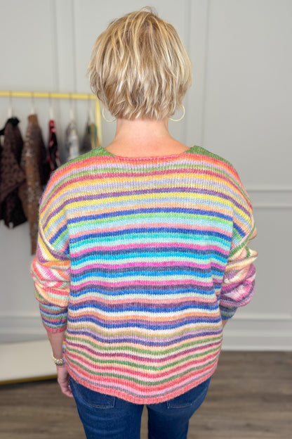 Back view of woman wearing Swagger Boutique’s Multi Striped Sweater with jeans with clothing hanging in the background.
