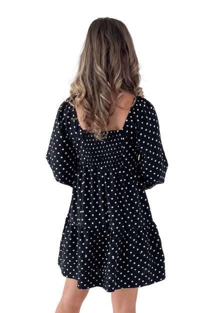 Back view of woman wearing polka dot dress and boots against white studio background.