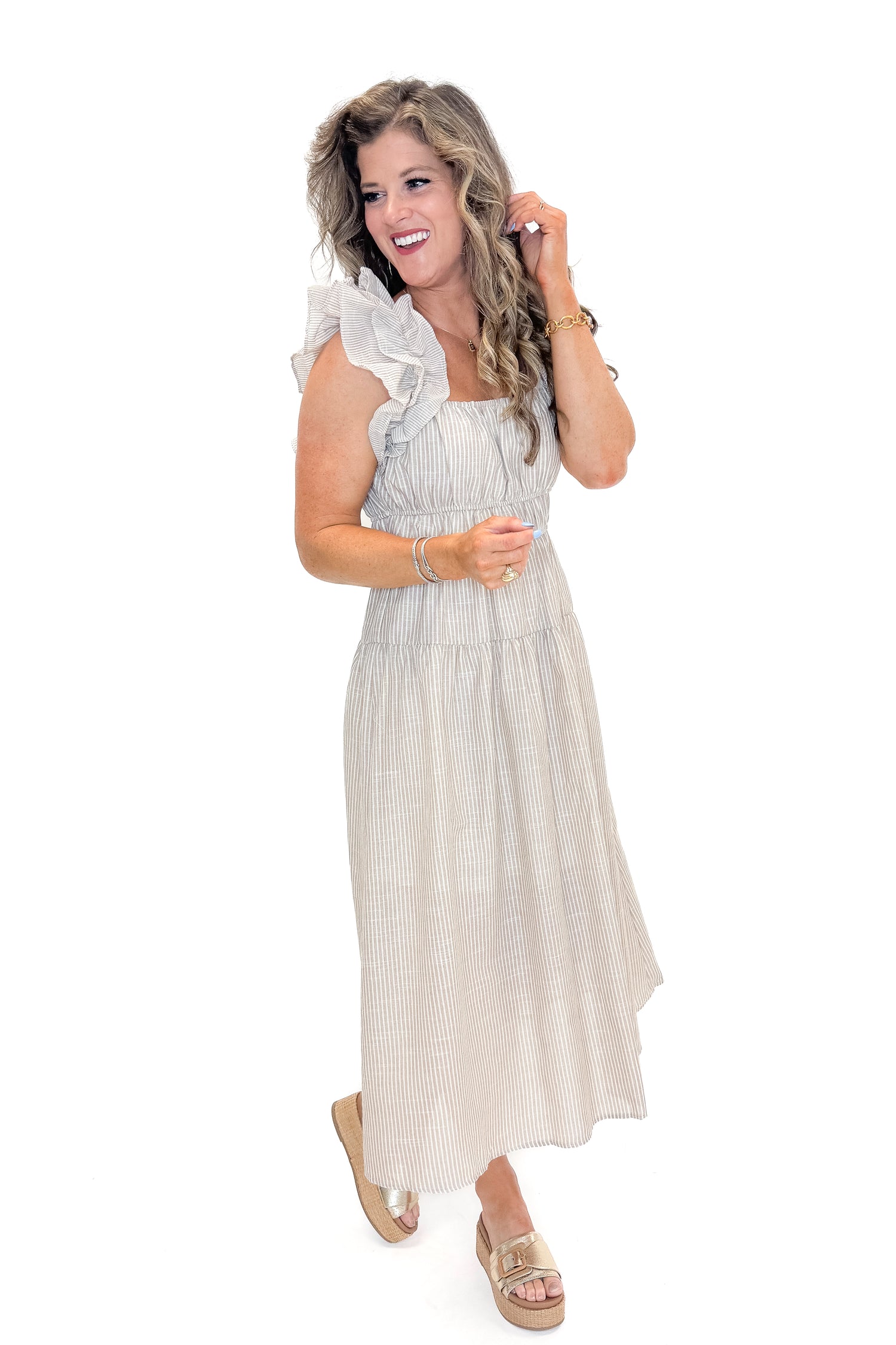 Side view of woman wearing Taupe Striped Ruffle Strap Midi Dress with sandals against white studio background.