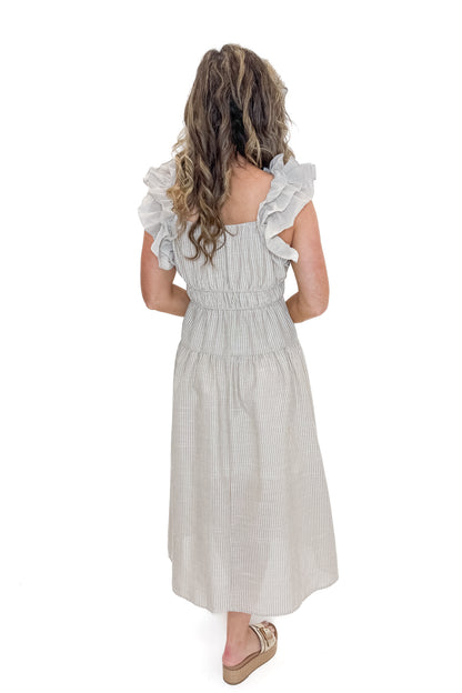 Back view of woman wearing Taupe Striped Ruffle Strap Midi Dress with sandals against white studio background.