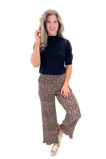 Front view of woman wearing Leopard Pleated Pants with sweater against white studio background.