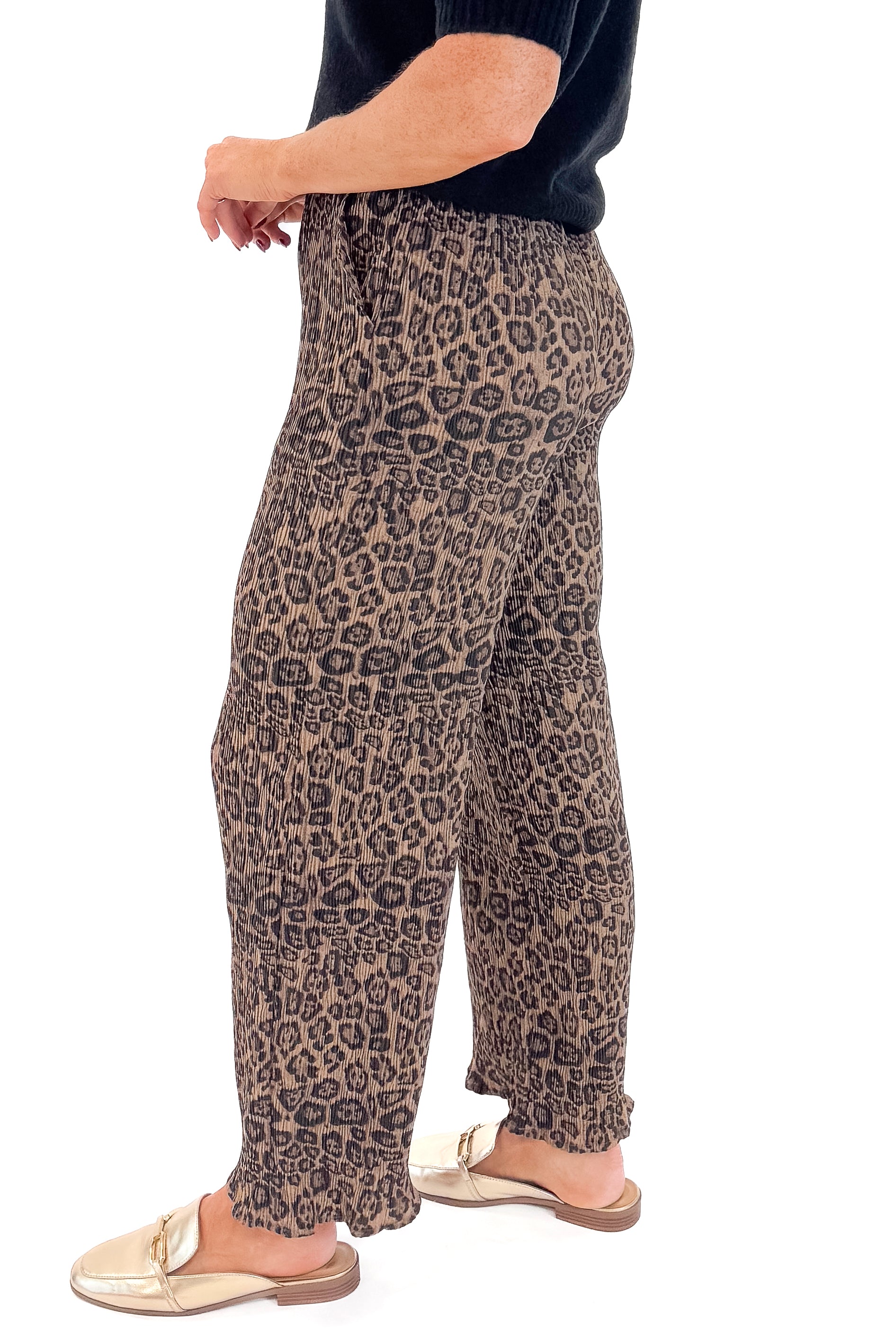 Side view of woman wearing Leopard Pleated Pants with sweater against white studio background.