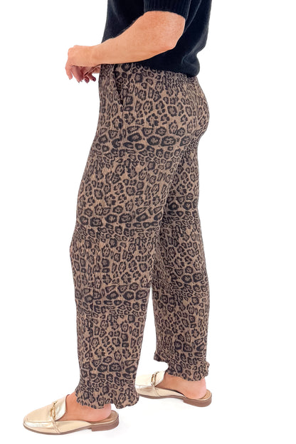 Side view of woman wearing Leopard Pleated Pants with sweater against white studio background.