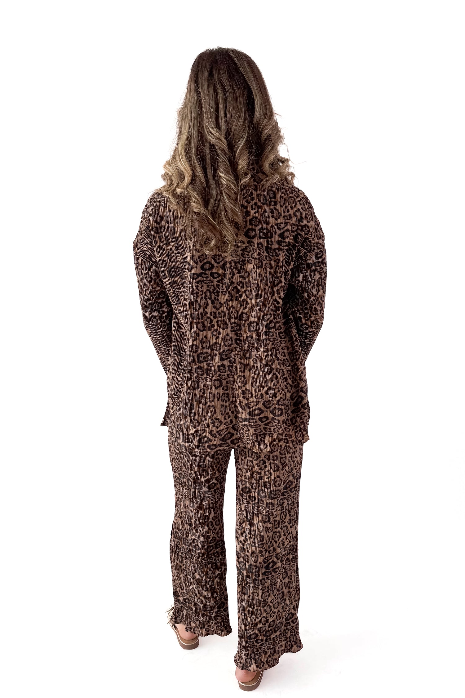 Back view of woman wearing Leopard Pleated Pants with matching top against white studio background.