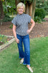 Front view of woman wearing Grey Leopard Short Sleeve Fuzzy Top and blue jeans outside with greenery and trees.
