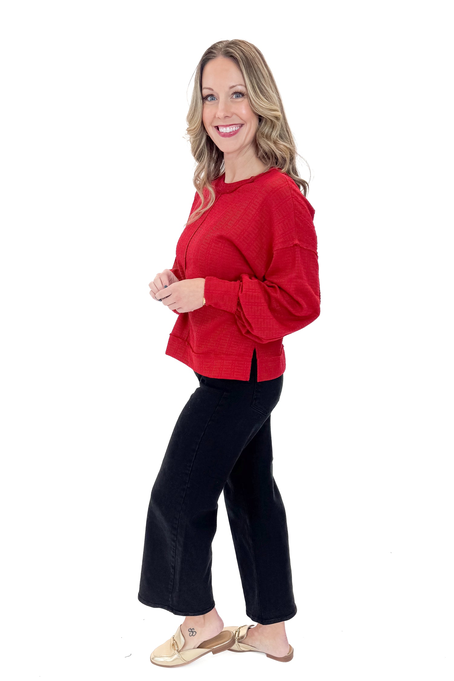 Side view of woman wearing Red Center Seam Textured Top with jeans against white studio background.