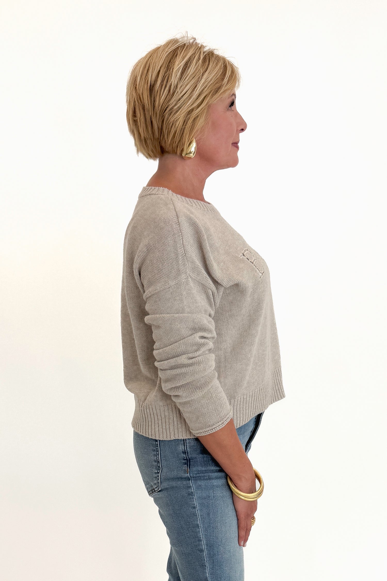 Side view of woman wearing Swagger Boutique’s Natural Heather Beach Embroidered Sweater by Z Supply with jeans against white studio background.