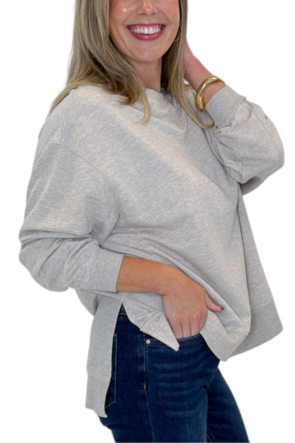 A woman wearing a light heather gray long-sleeve crewneck sweatshirt and dark blue jeans, shown from the chest down against a plain white background.