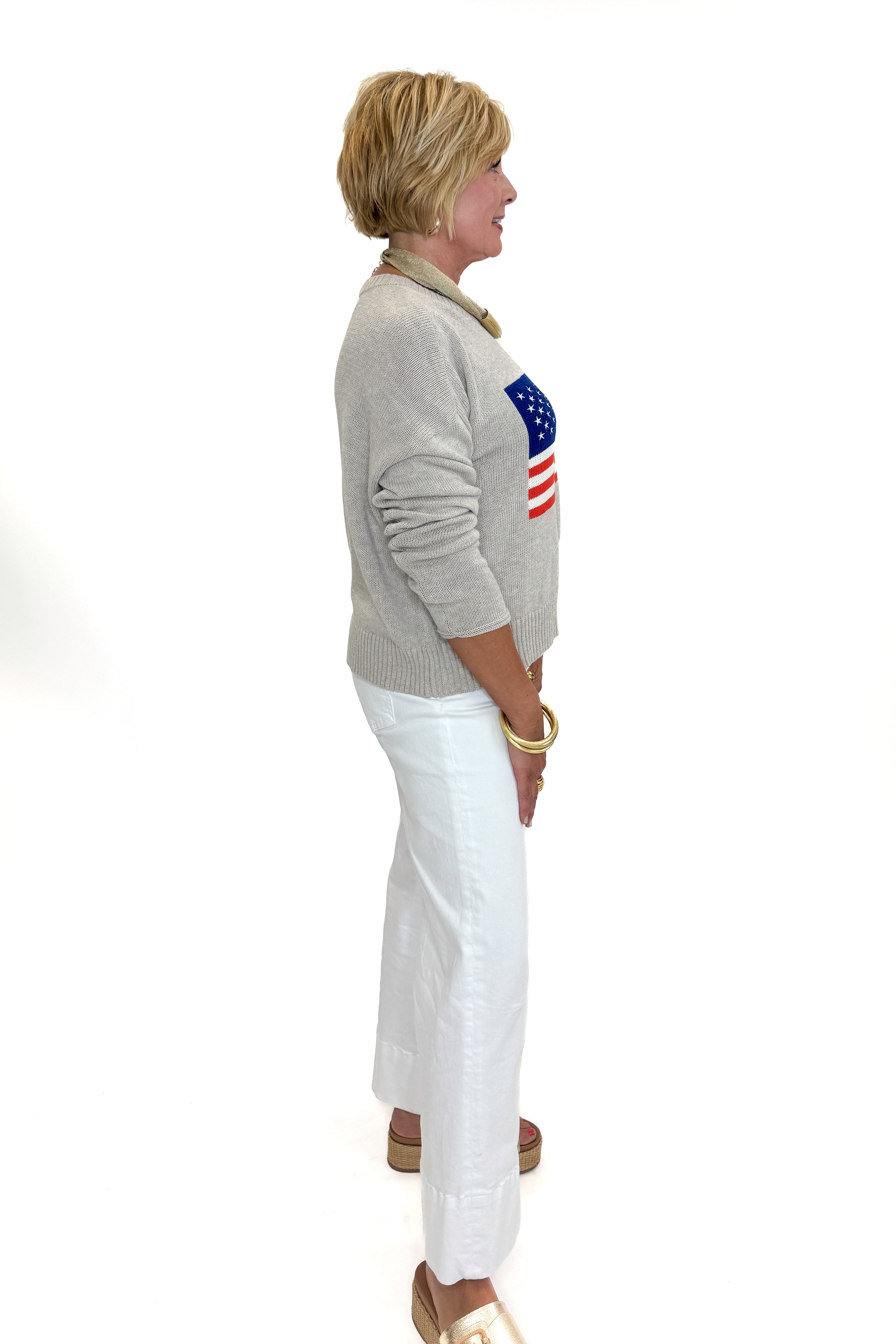 Side view of woman wearing Swagger Boutique’s Sienna Patriot Sweater In Natural Heather by Z Supply with jeans against white studio background. 