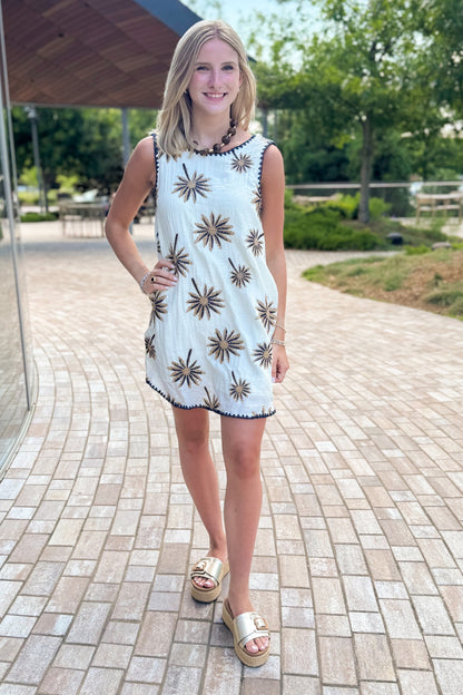 Front view of woman wearing Swagger Boutique’s Natural Palm Embroidered Shift Mini Dress with sandals walking at a park.