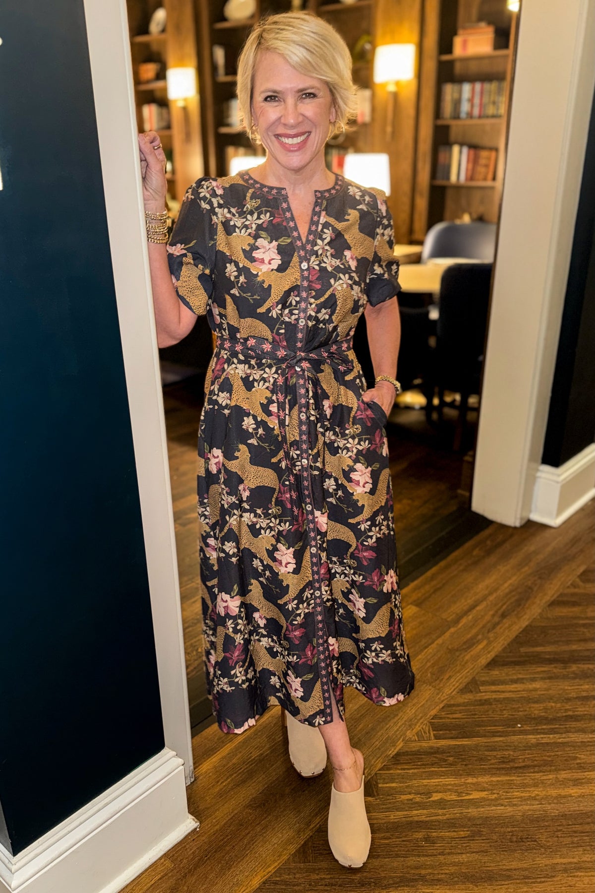 Front view of woman wearing Swagger Boutique’s Navy Animal Print Midi Dress with clogs standing outside of a den.