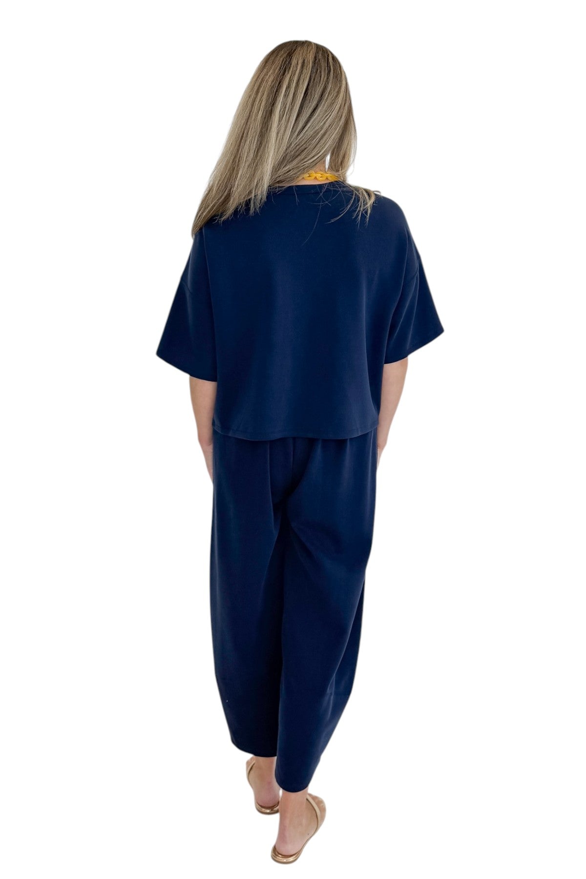 Back view of woman wearing Swagger Boutique’s Navy Barrel Lounge Pants with Navy Round Neck Short Sleeve Top against white studio background.