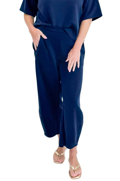 Front detail view of woman wearing Swagger Boutique’s Navy Barrel Lounge Pants with Navy Round Neck Short Sleeve Top against white studio background.