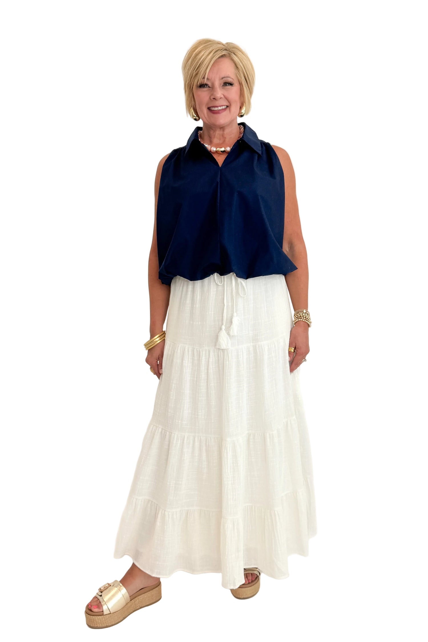 Front view of woman wearing Swagger Boutique’s Navy Bubble Hem Collared Sleeveless Top with Just A Consideration White Flowy Tiered Cotton Skirt against white studio background.
