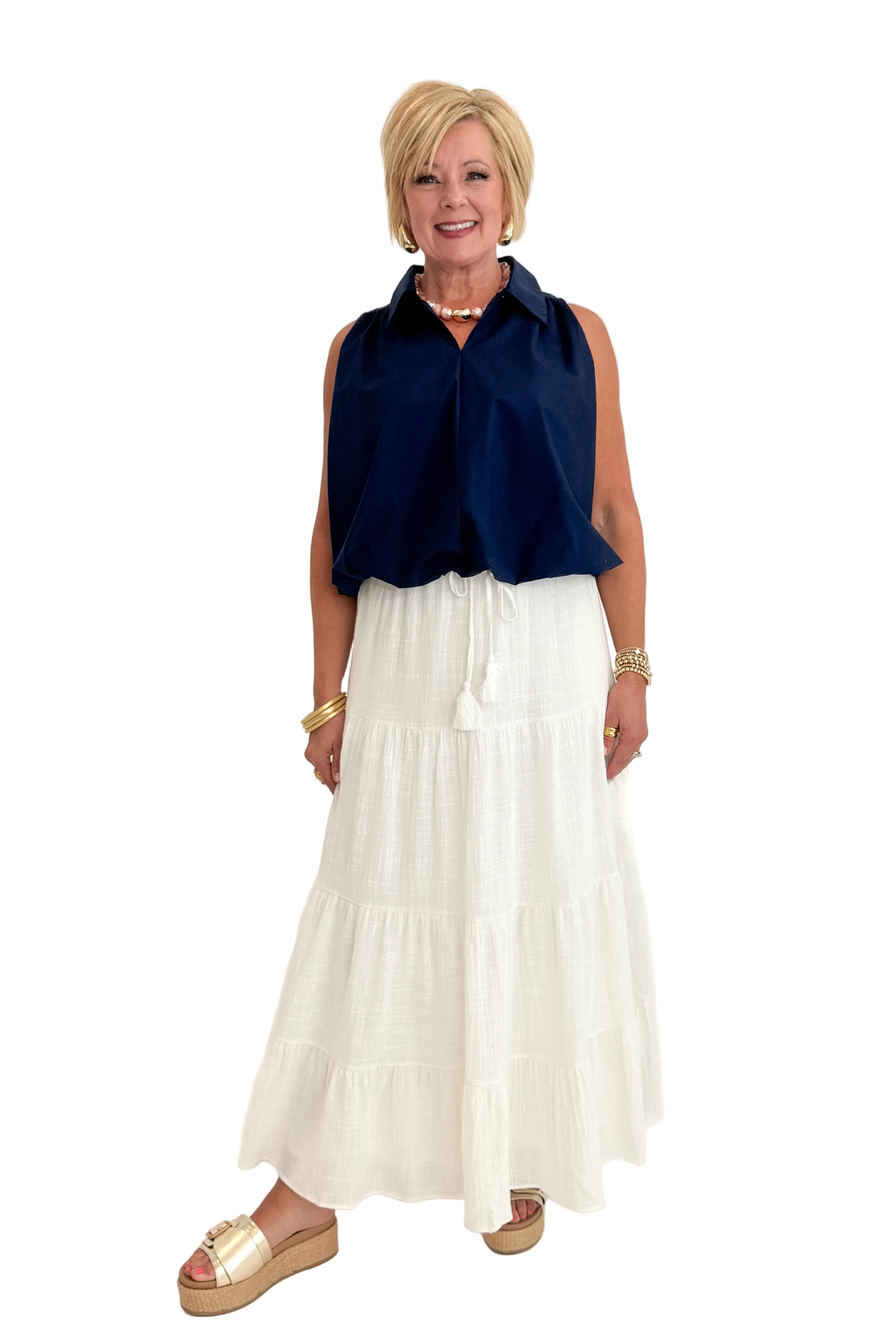 Front view of woman wearing Swagger Boutique’s Navy Bubble Hem Collared Sleeveless Top with Just A Consideration White Flowy Tiered Cotton Skirt against white studio background.