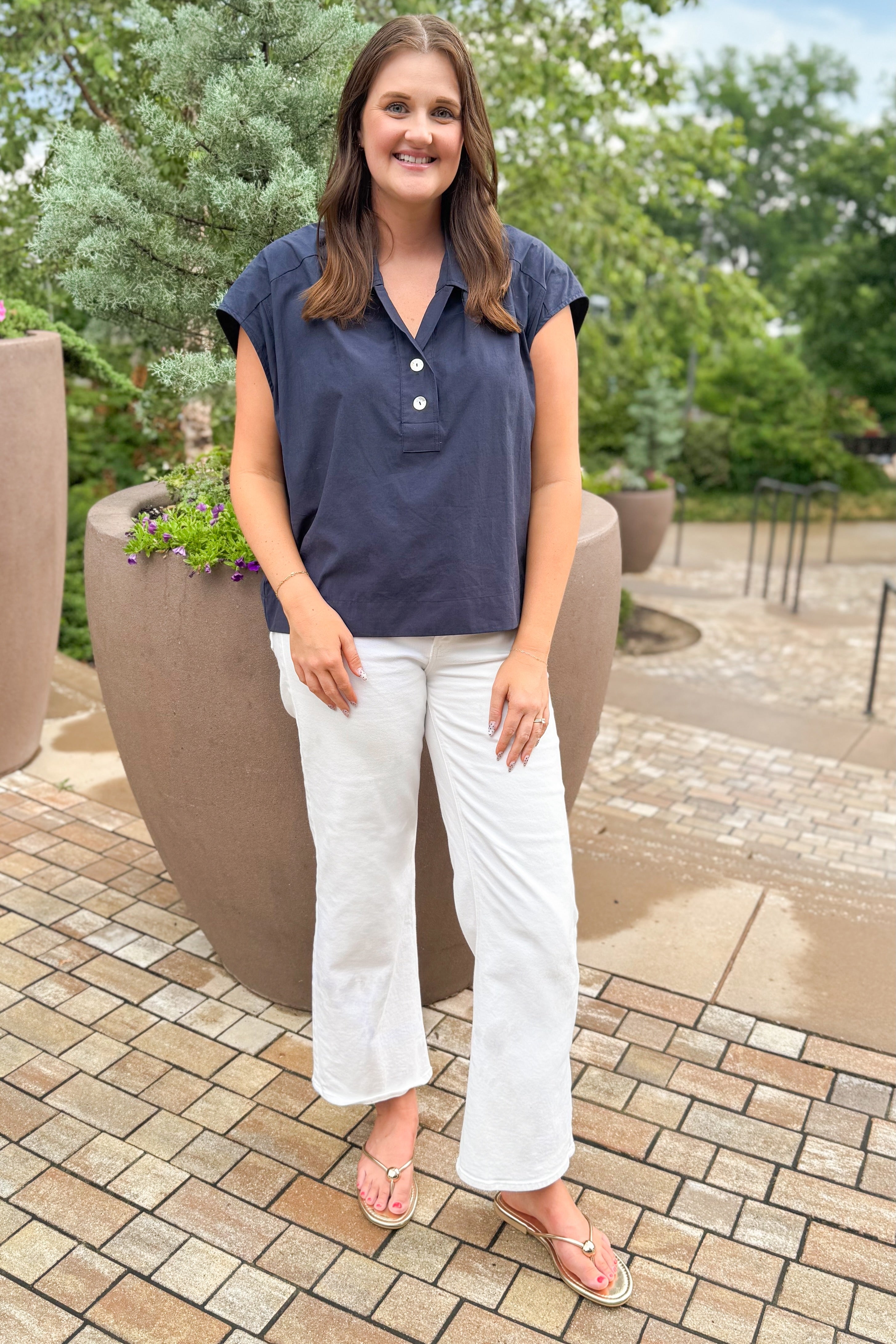 Front view of woman wearing Swagger Boutique’s Navy Collared Cap Sleeve Top  with jeans standing outside at a park.