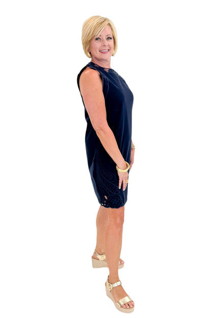 Side view of woman wearing Swagger Boutique’s Navy Embroidered Trim Mini Dress with sandals against white studio background.