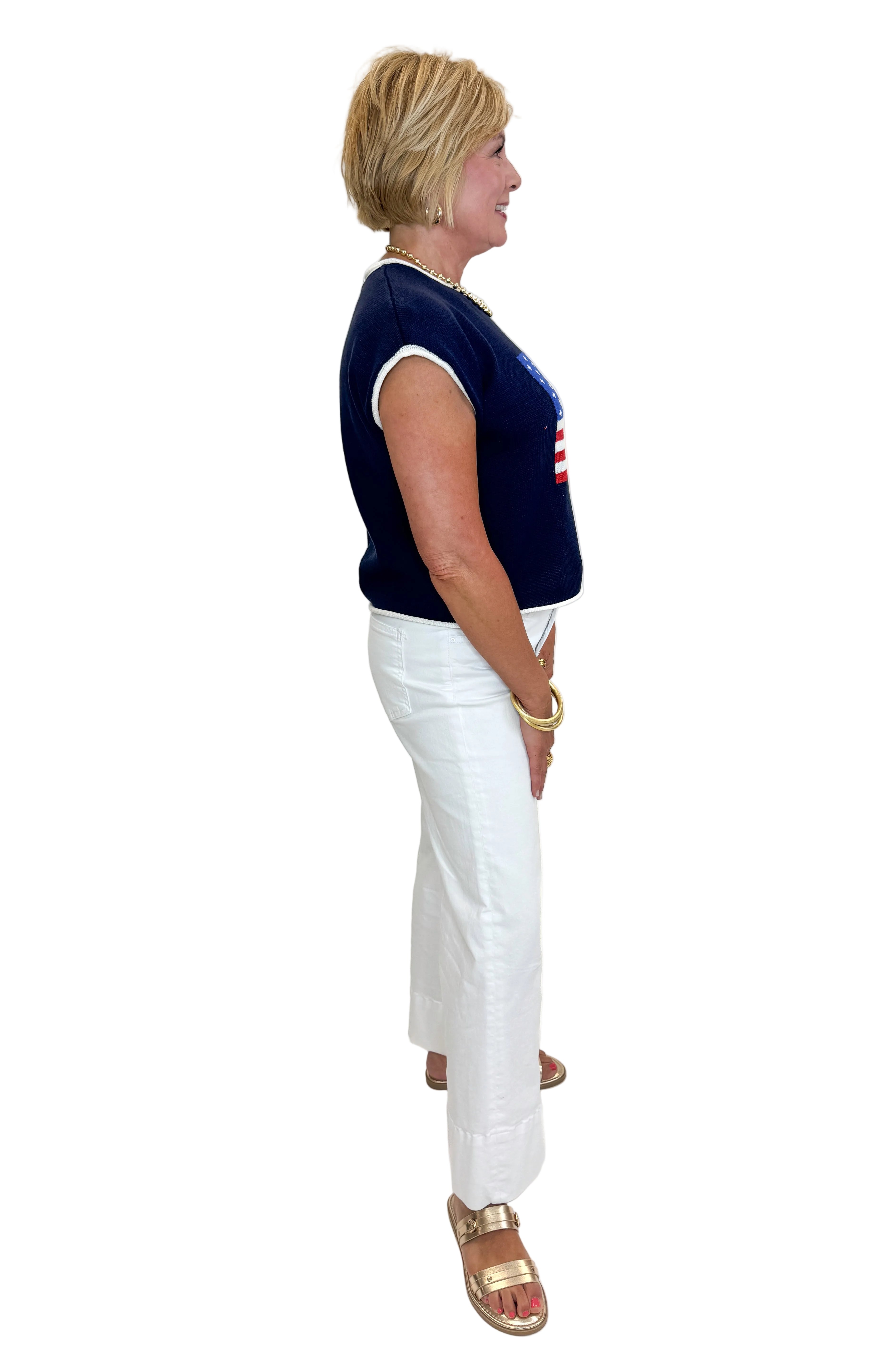 Side view of woman wearing Swagger Boutique’s Right On Cue Navy Flag Short Sleeve Sweater with jeans against white studio background.