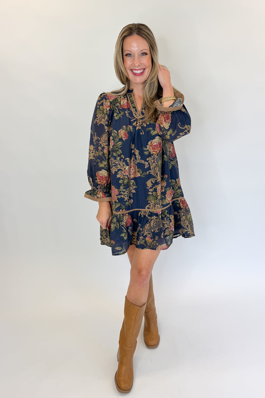 Front view of woman wearing Swagger Boutique’s Navy Floral Print Mini Dress with boots against white studio background.