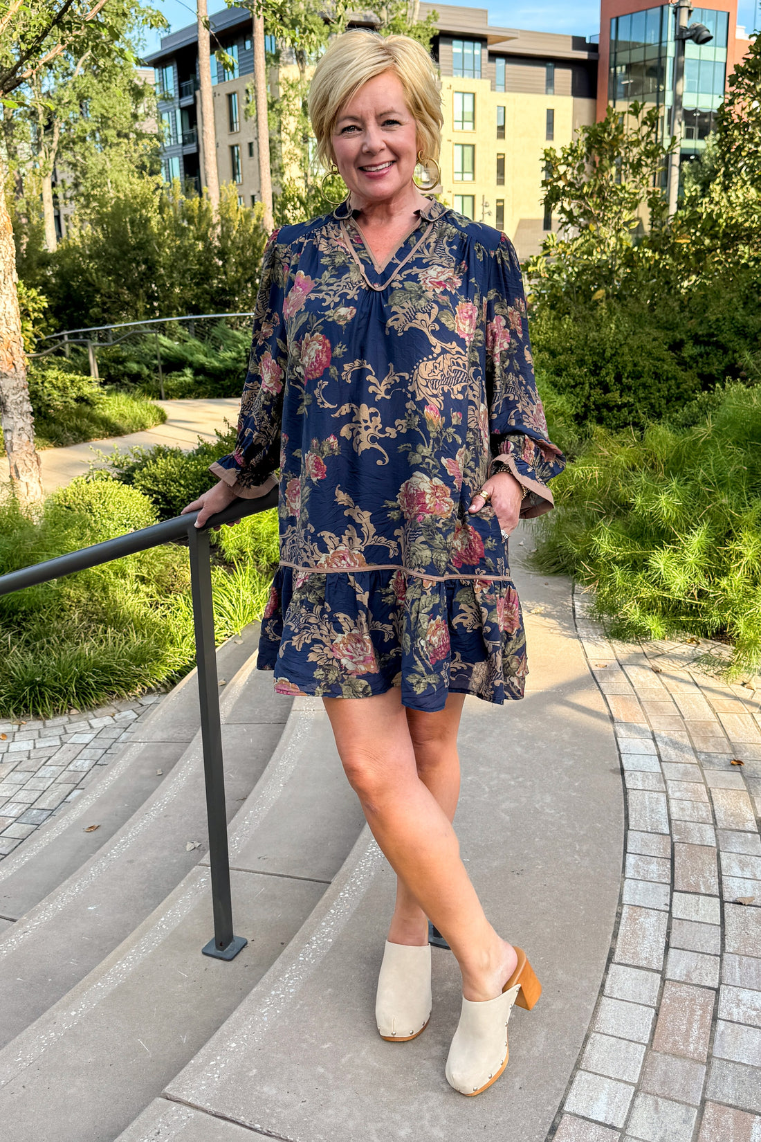Front view of woman wearing Swagger Boutique’s Navy Floral Print Mini Dress standing outside by stairs.