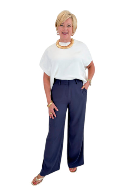 Front view of woman wearing Swagger Boutique’s Ivory Light Weight Short Sleeve Sweater with Navy High Waisted Trousers by Skies Are Blue against white studio background.