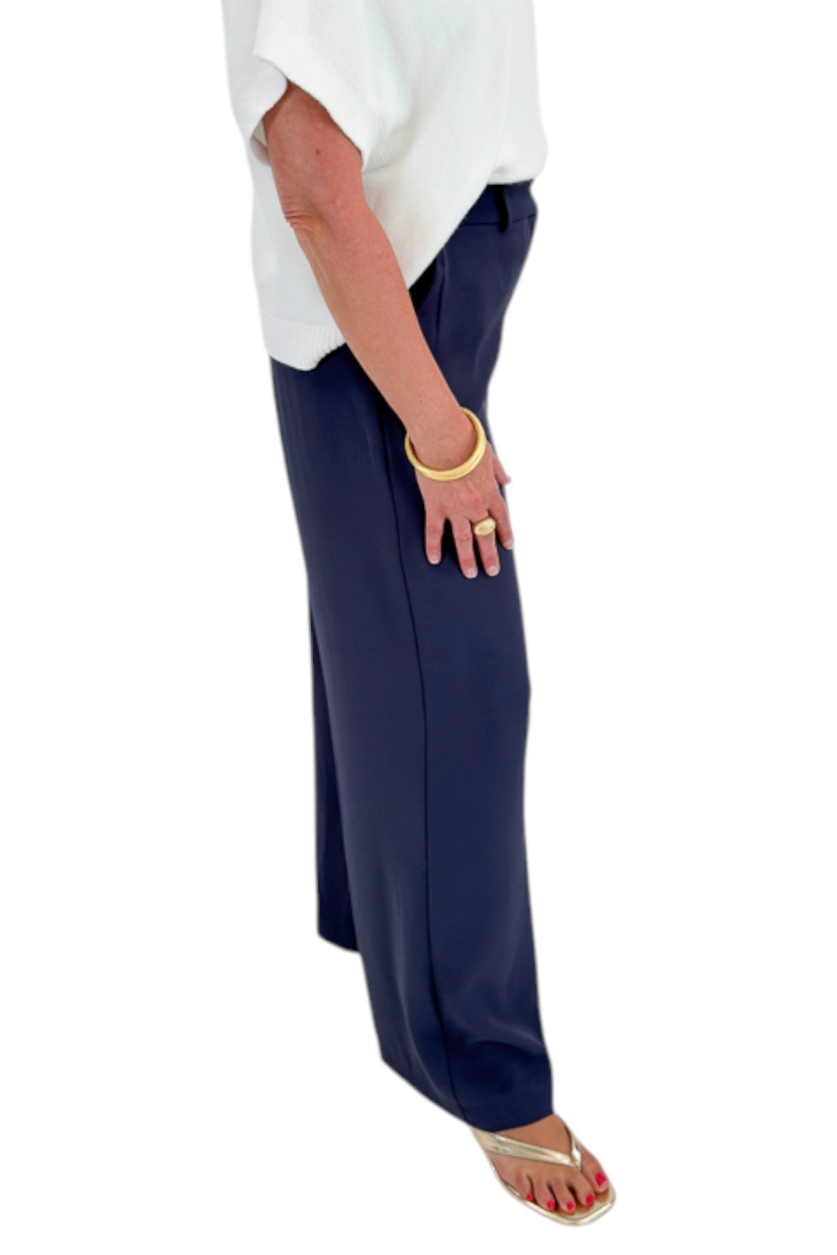 Side detail view of woman wearing Swagger Boutique’s Ivory Light Weight Short Sleeve Sweater with Navy High Waisted Trousers by Skies Are Blue against white studio background.
