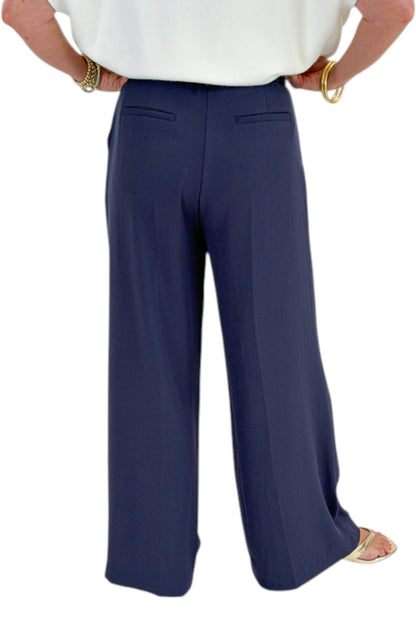 Back detail view of woman wearing Swagger Boutique’s Ivory Light Weight Short Sleeve Sweater with Navy High Waisted Trousers by Skies Are Blue against white studio background.
