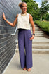 Front view of woman wearing Swagger Boutique’s Ecru Horsebit Buckle Tank by Entro with Navy High Waisted Trousers by Skies Are Blue standing against a brick wall.