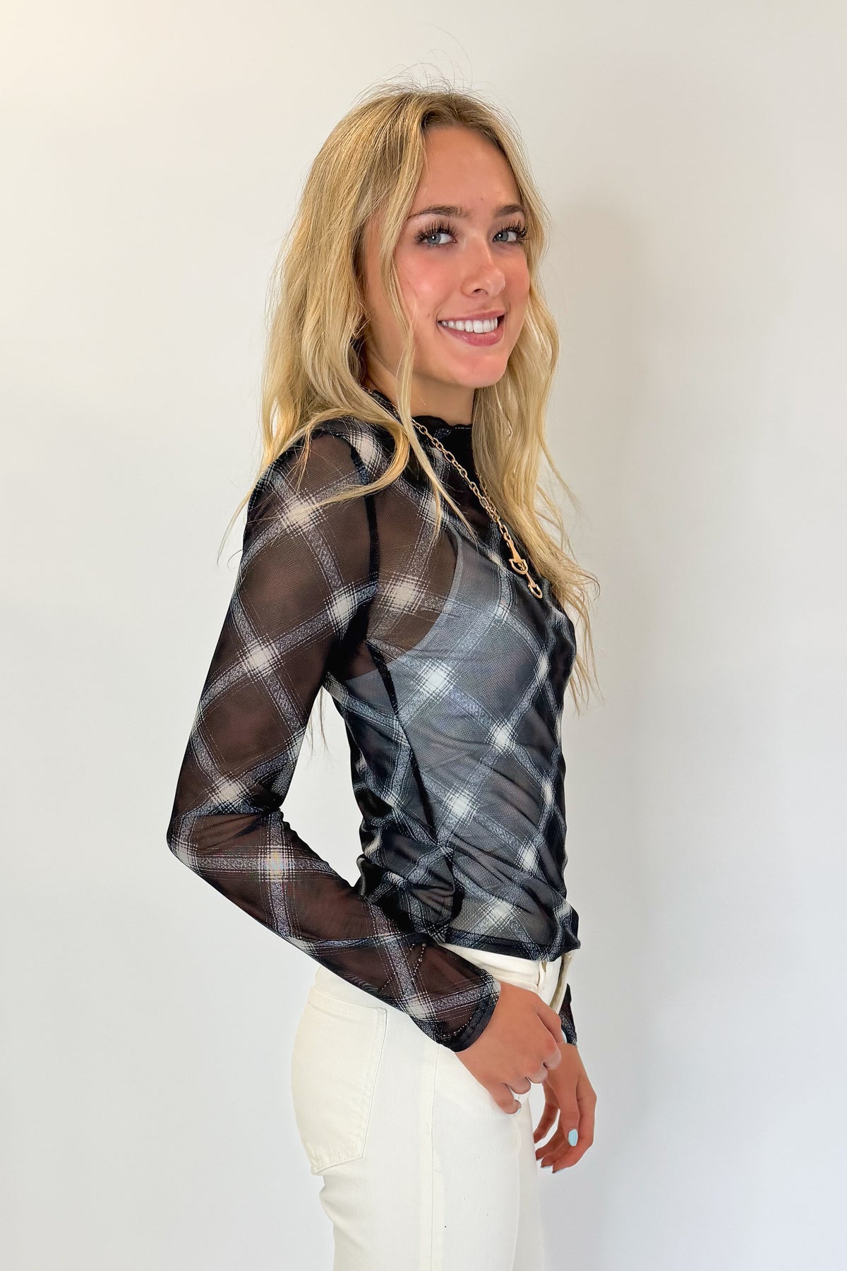 Side view of woman wearing Swagger Boutique’s Navy Plaid Mesh Top with jeans against white studio background.
