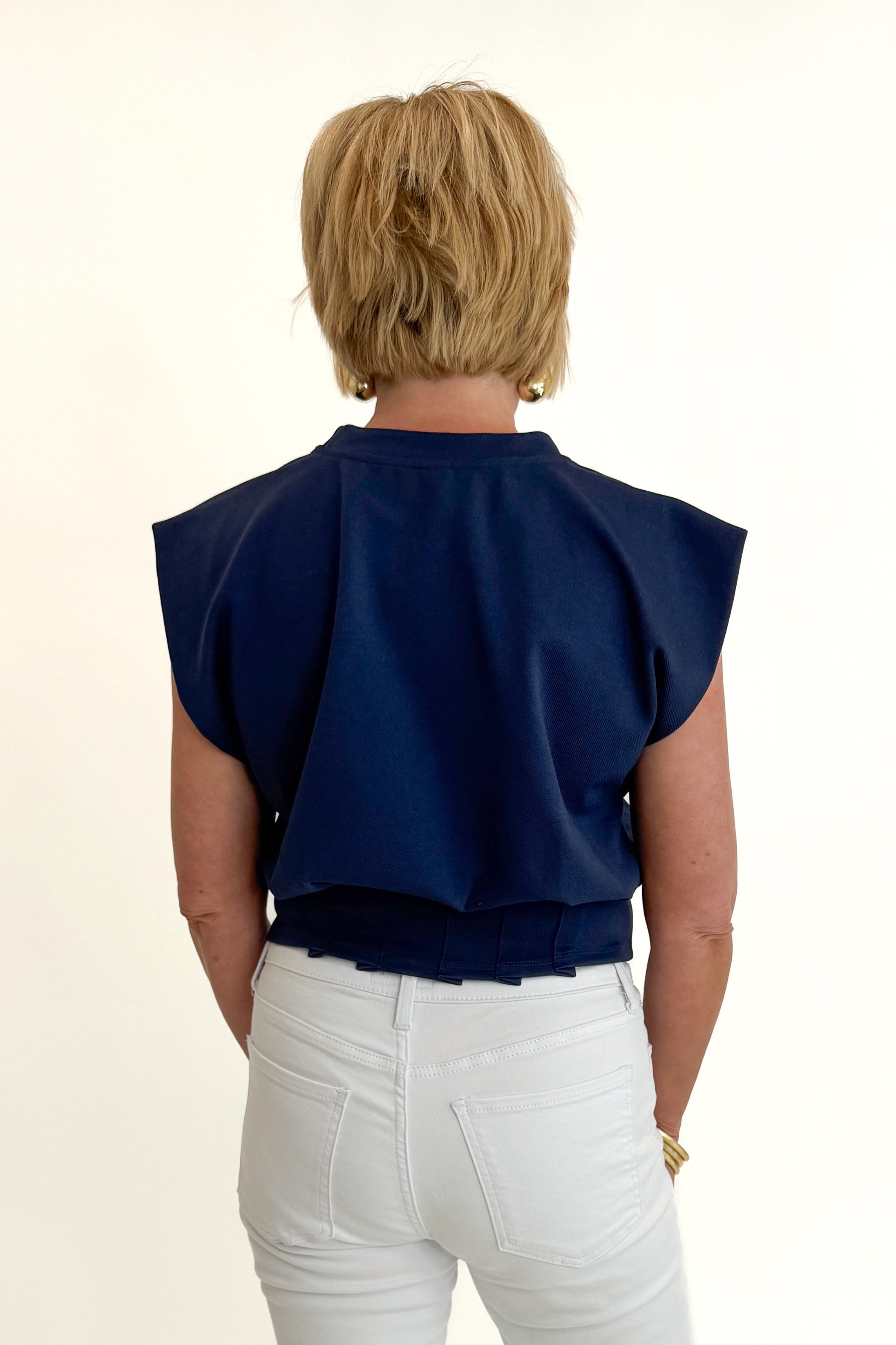 Back view of woman wearing Swagger Boutique’s Navy Pleat Detail Tank with jeans against white studio background.