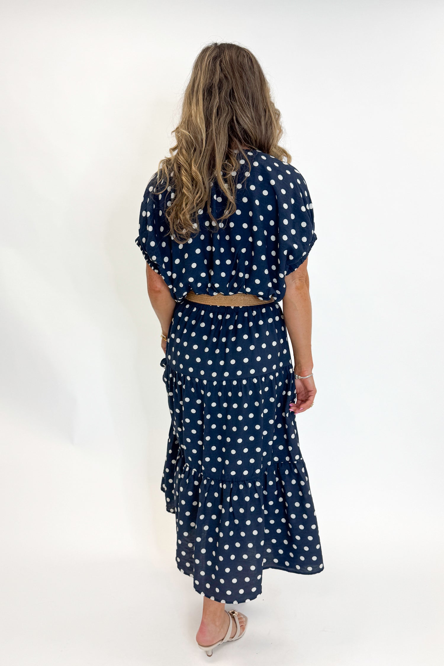 Back view of woman wearing Swagger Boutique’s Navy Polka Dot Bubble Hem Top by Entro with matching Navy Polka Dot Tiered Skirt by Entro against white studio background.