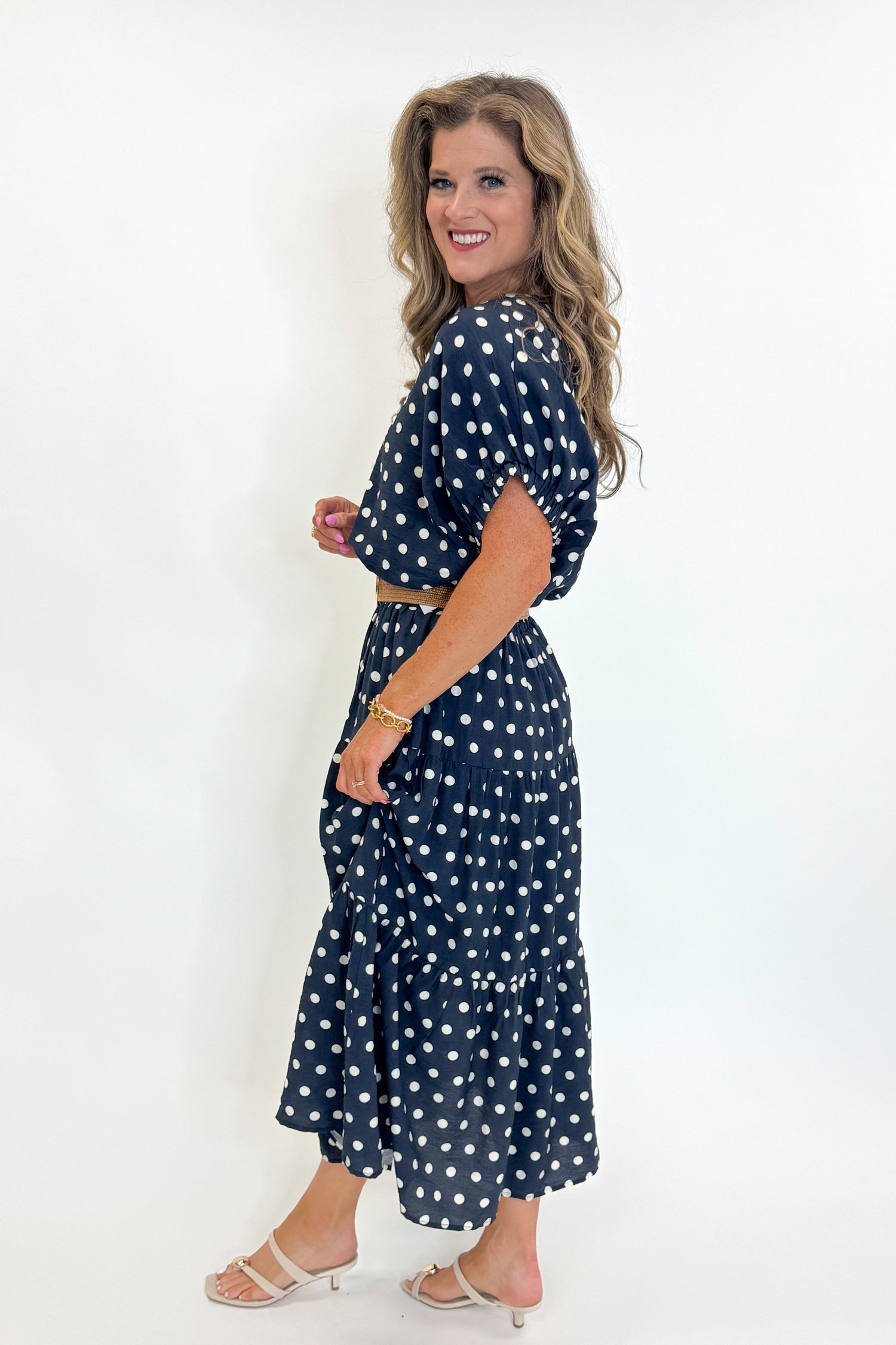 Side view of woman wearing Swagger Boutique’s Navy Polka Dot Bubble Hem Top by Entro with matching Navy Polka Dot Tiered Skirt by Entro against white studio background.