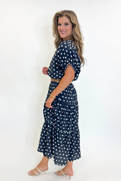 Side view of woman wearing Swagger Boutique’s Navy Polka Dot Bubble Hem Top by Entro with matching Navy Polka Dot Tiered Skirt by Entro against white studio background.