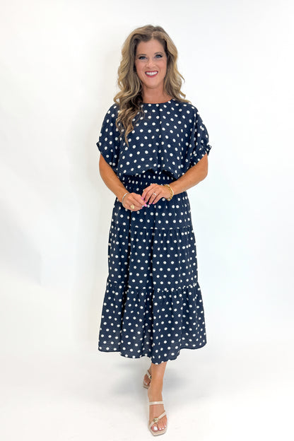 Front view of woman wearing Swagger Boutique’s Navy Polka Dot Bubble Hem Top by Entro with matching Navy Polka Dot Tiered Skirt by Entro against white studio background.