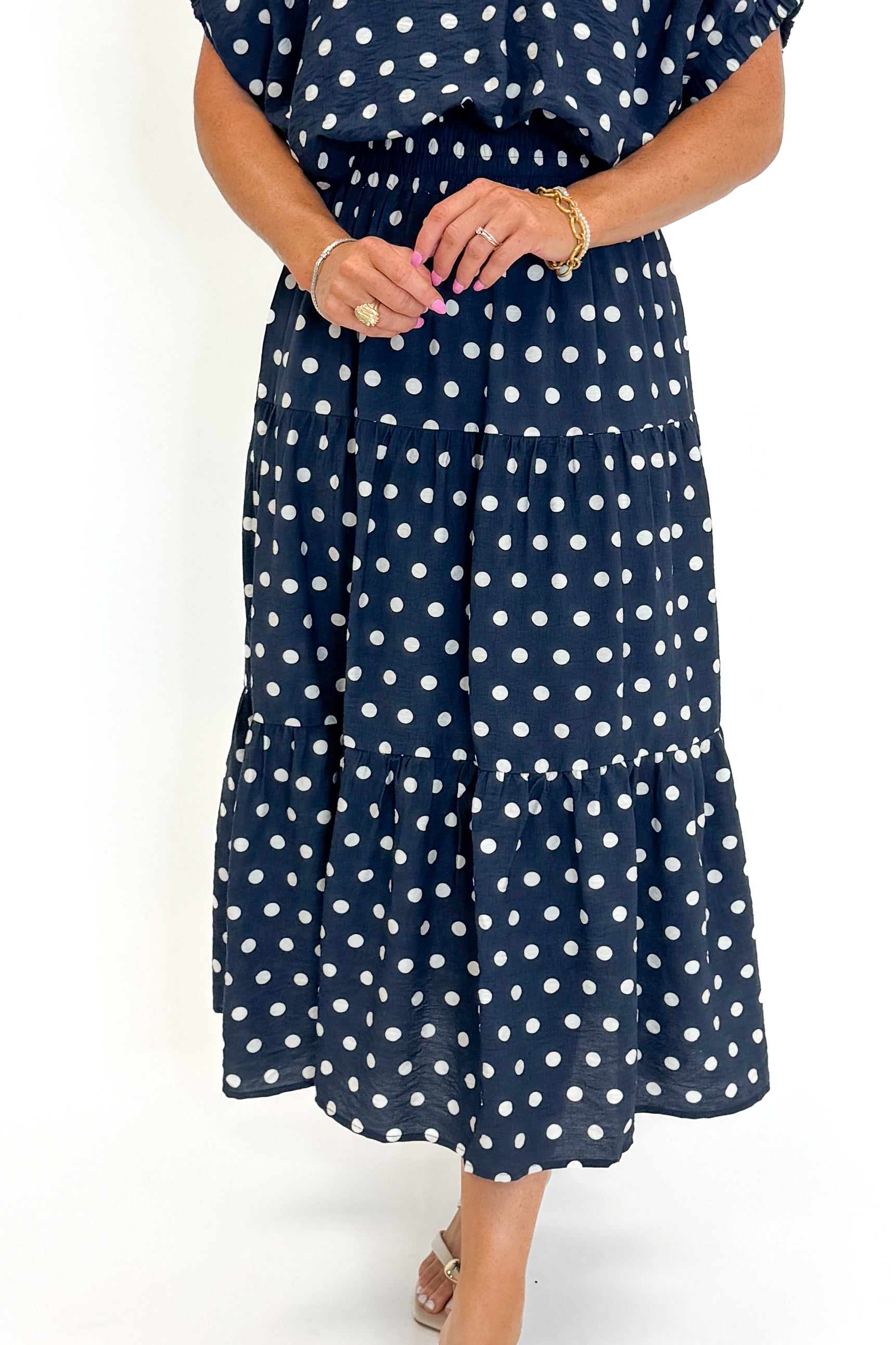 Front detail view of woman wearing Swagger Boutique’s Navy Polka Dot Bubble Hem Top by Entro with matching Navy Polka Dot Tiered Skirt by Entro against white studio background.