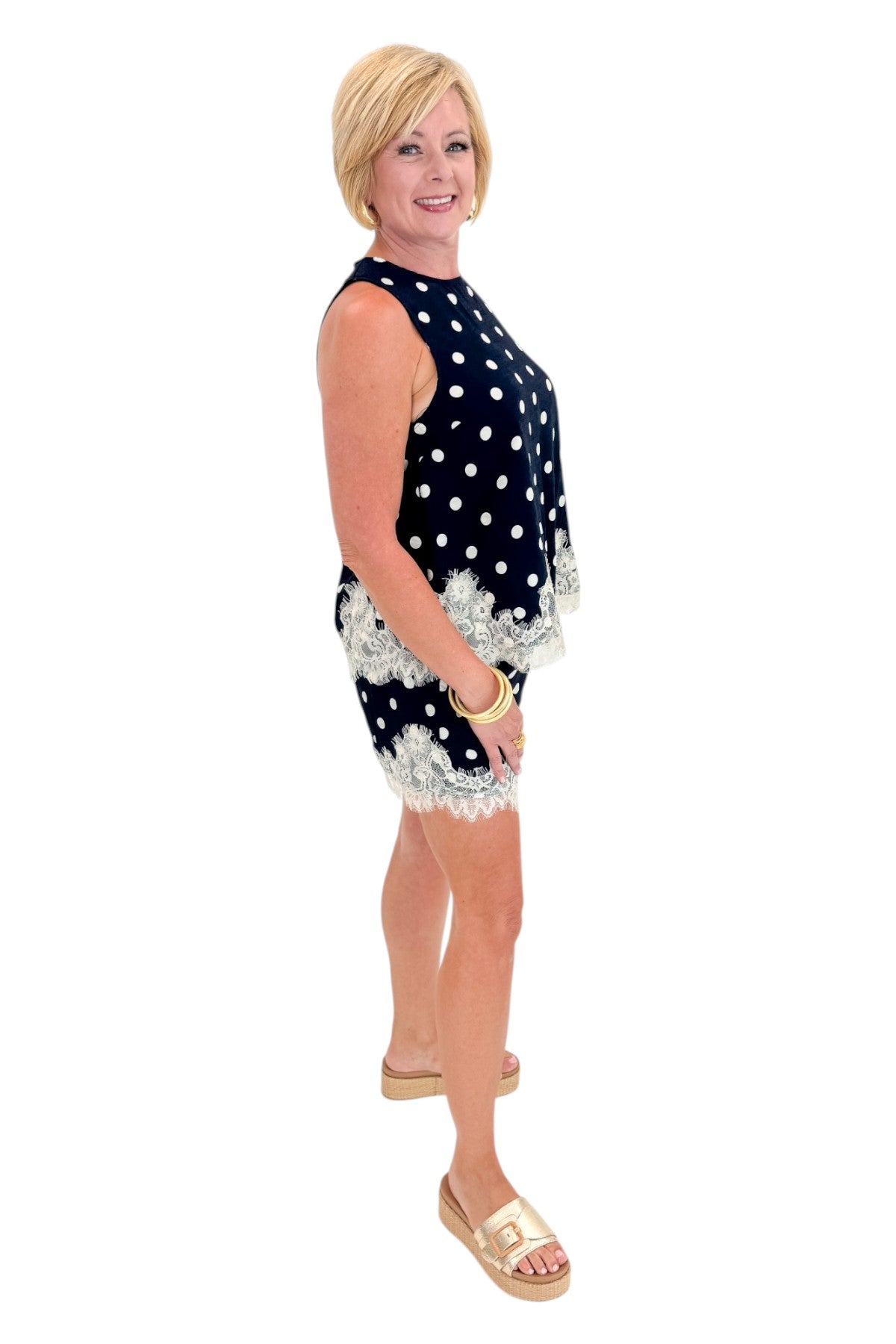 Side view of woman wearing Swagger Boutique’s Navy Polka Dot Lace Trim Shorts by Entro with matching tank against white studio background.