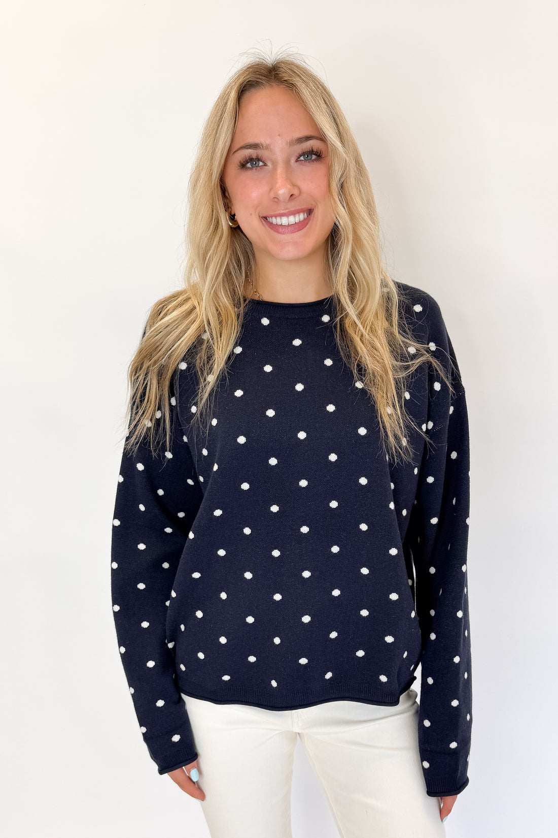 Front view of woman wearing Swagger Boutique’s Navy Polka Dot Sweater with jeans against white studio background.
