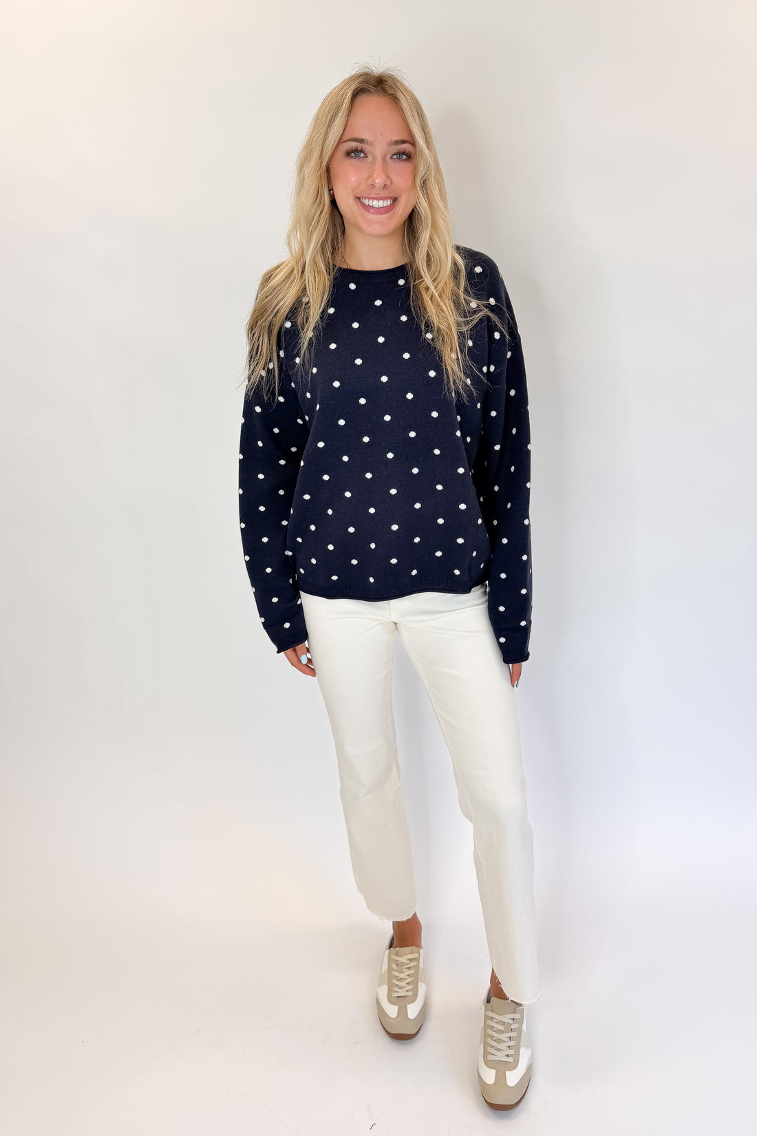 Front view of woman wearing Swagger Boutique’s Navy Polka Dot Sweater with jeans against white studio background.