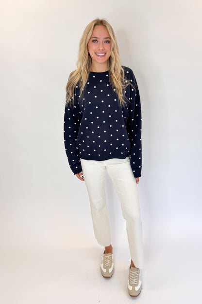 Front view of woman wearing Swagger Boutique’s Navy Polka Dot Sweater with jeans against white studio background.