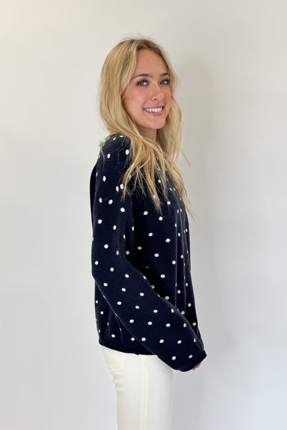 Side view of woman wearing Swagger Boutique’s Navy Polka Dot Sweater with jeans against white studio background.