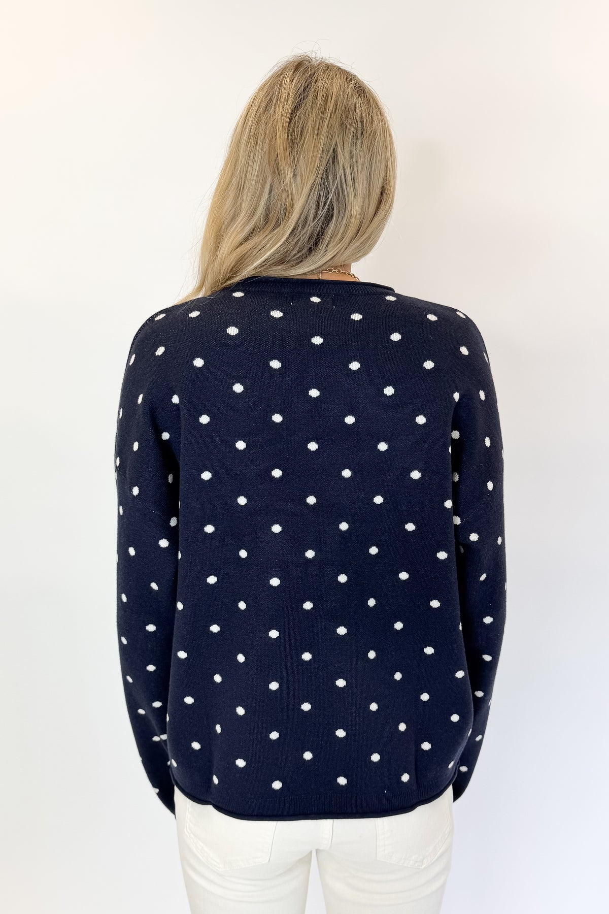 Back view of woman wearing Swagger Boutique’s Navy Polka Dot Sweater with jeans against white studio background.