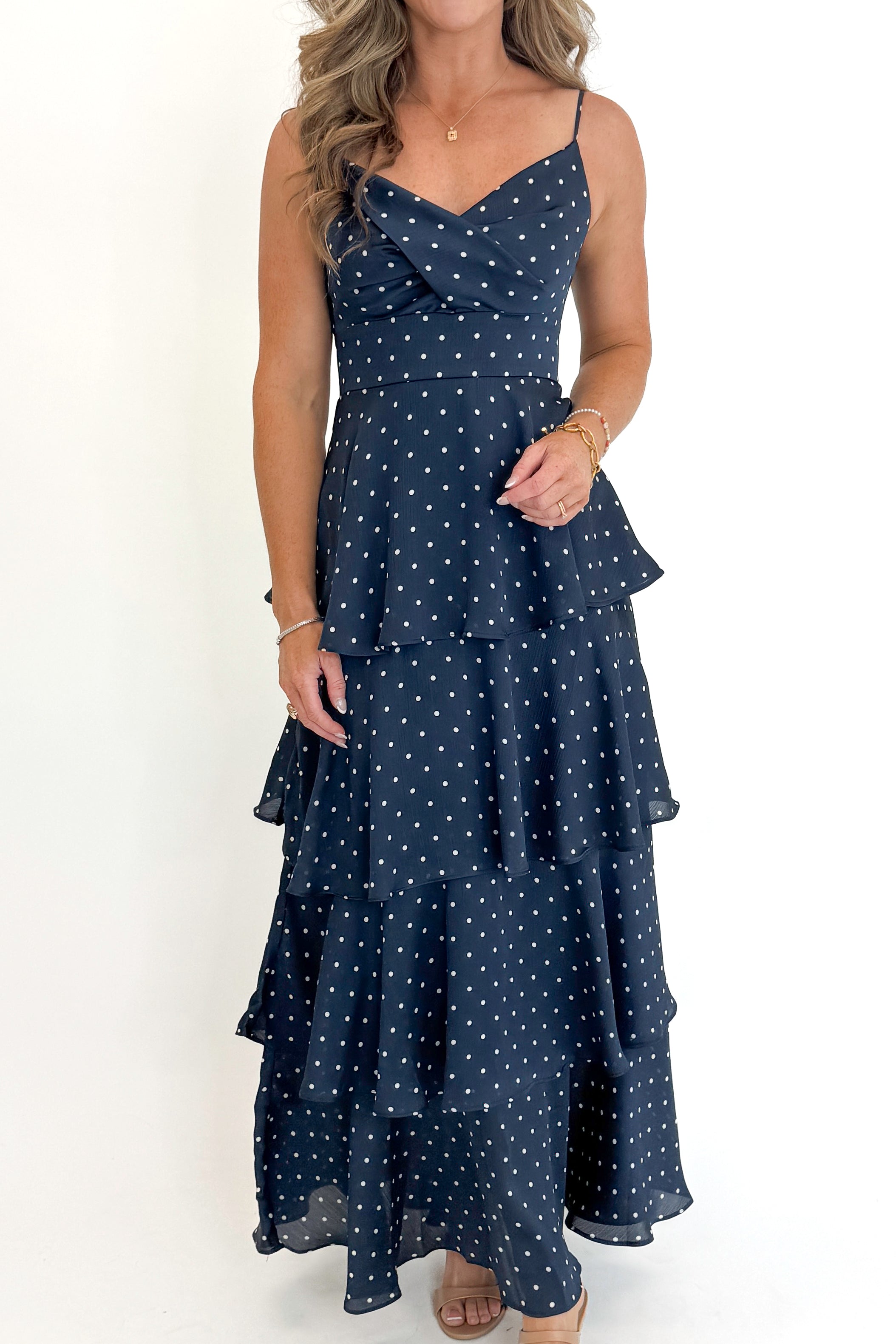 Front detail view of woman wearing Swagger Boutique’s Navy Polka Dot Tiered Maxi Dress against white studio background.