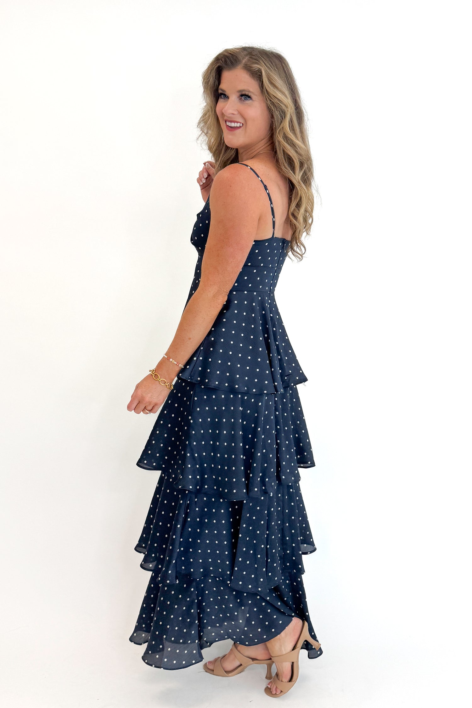 Side view of woman wearing Swagger Boutique’s Navy Polka Dot Tiered Maxi Dress against white studio background.