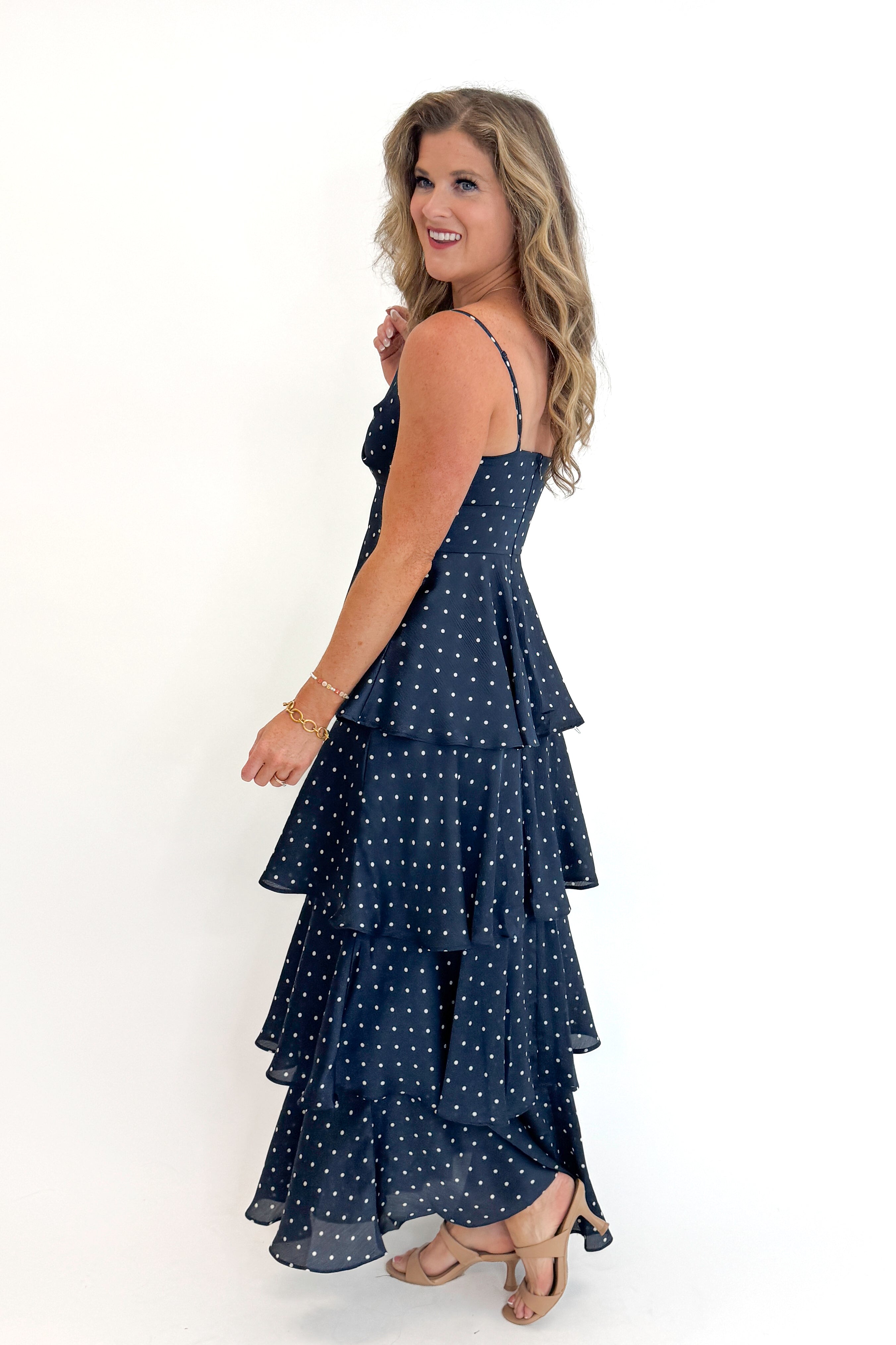 Side view of woman wearing Swagger Boutique’s Navy Polka Dot Tiered Maxi Dress against white studio background.