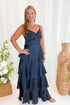 Front view of woman wearing Swagger Boutique’s Navy Polka Dot Tiered Maxi Dress against decorative background.